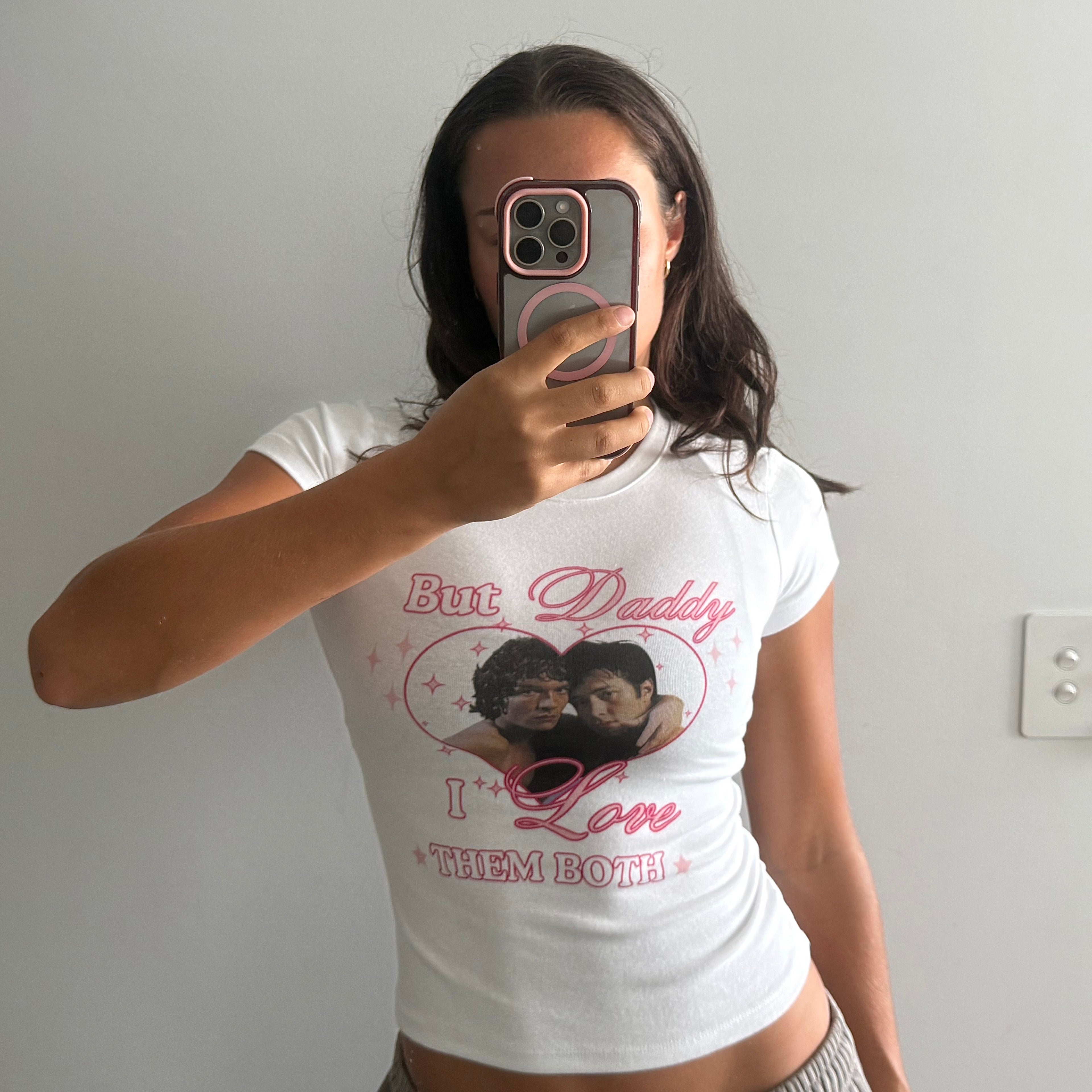 Person wearing a white t-shirt with graphic design and text, taking a mirror selfie.